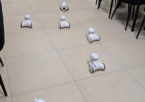 Roboty jeżdżą po podłodze, w tle siedzą dzieci
