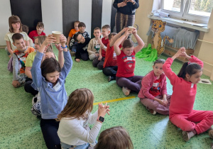 Dzieci siedzą w 2 rzędach i podają kubek z wodą