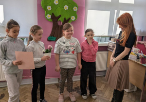 Dziewczynki wręczają kwiatka i dyplom kobiecie