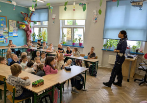 dzieci siedzą w ławkach słuchając policjantki