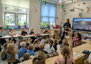 dzieci siedzą w ławkach słuchając policjantki