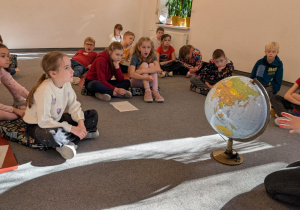 Uczniowie siedzą na podłodze i patrzą na globus