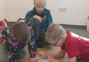 Uczniowie siedzą na podłodze i rozwiązują zadanie