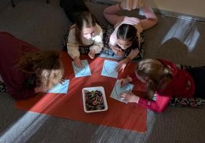 Uczniowie siedzą na podłodze i rysyją