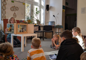 Uczniowie siedzą na podłodze i słuchają bajki w terzyku kamishibai