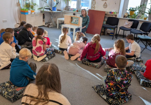 Uczniowie siedzą na podłodze i słuchają bajki