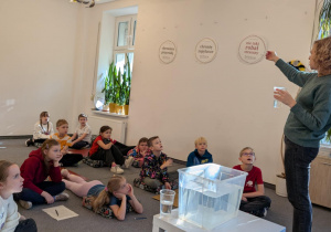 Uczniowie siedzą na podłodze i uczestniczą w eksperymencie nt wody pitnej