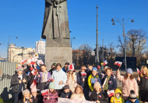 dzieci pozują do zdjęcia pod pomnikiem marszałka Piłsudskiego