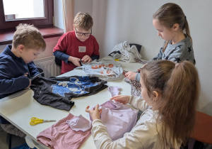 Dzieci siedzą przy stoliku i tworzą torby z koszulek