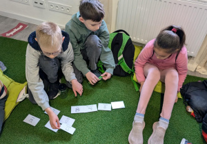 Dzieci siedząc na podłodze rozwiązują ekologiczne zdanie