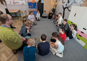 Mężczyzna z dziećmi siedzi na dywanie i objaśnia reguły gry