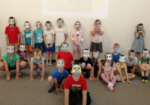 Dzieci w maskach stoja pod ścianą