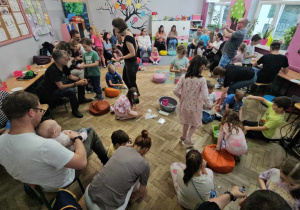 Dorośli z dziećmi siedzą i stoją w kole